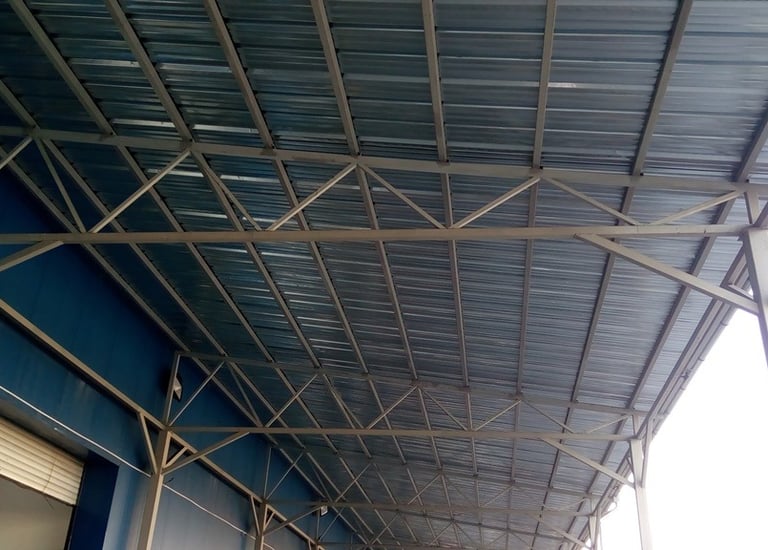 An underside view of a metal roof structure, showcasing corrugated galvanized iron sheets and a steel truss system, useful