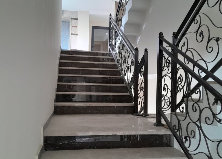 Modern interior staircase featuring dark marble steps and decorative wrought iron railings.