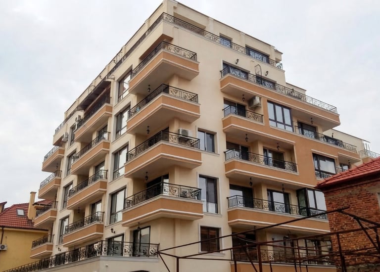 Modern multi-story apartment building with balconies and wrought iron railings under a cloudy sky.