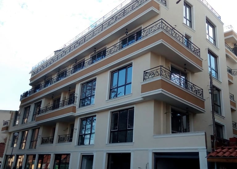 Modern multi-story apartment building with beige facade and decorative wrought iron balconies.