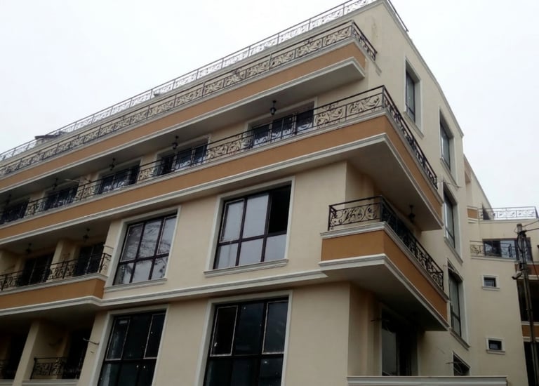 Modern multi-story apartment building with beige facade and decorative wrought iron balconies.