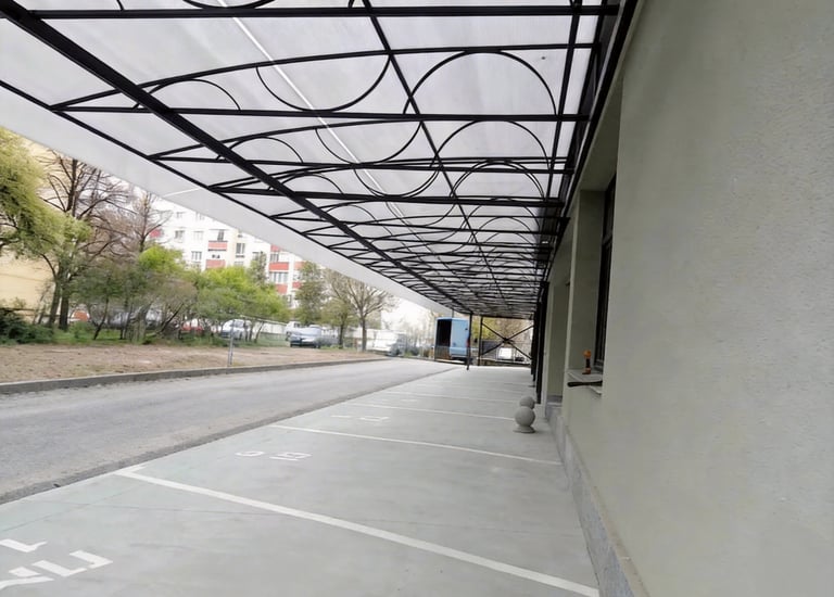 Modern polycarbonate canopy with decorative black metal frame over a sidewalk and parking area.