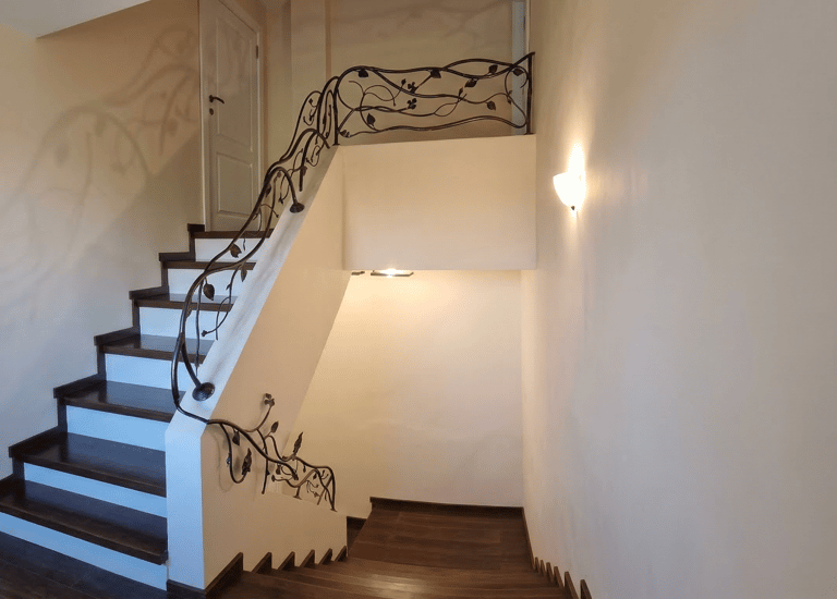 Modern wooden staircase featuring an ornate wrought iron railing with leaf and vine designs.
