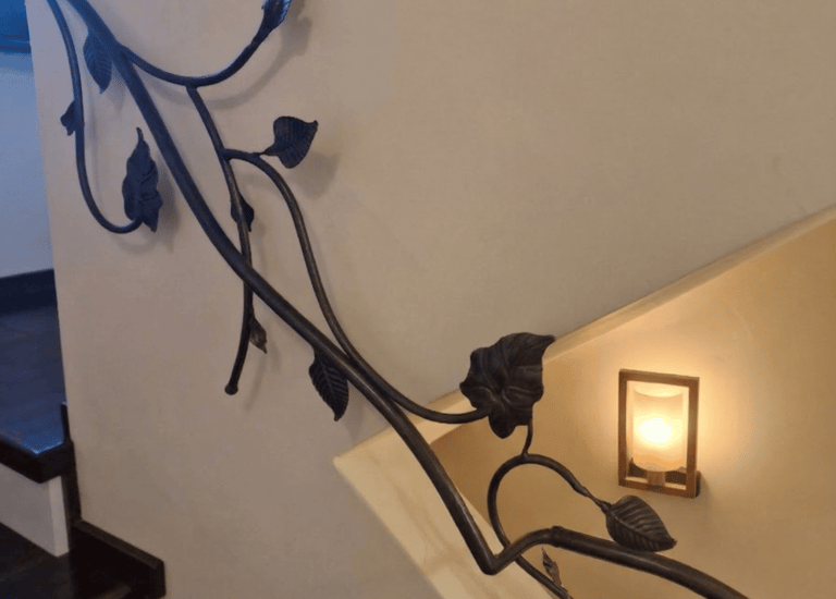 Custom wrought iron staircase railing with decorative vine and leaf design on a white wall.