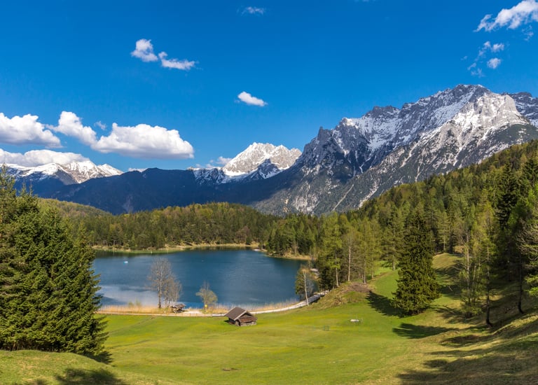 Scenic view of Lautersee lake in the Bavarian Alps with snow-capped mountains and evergreen pine forests.