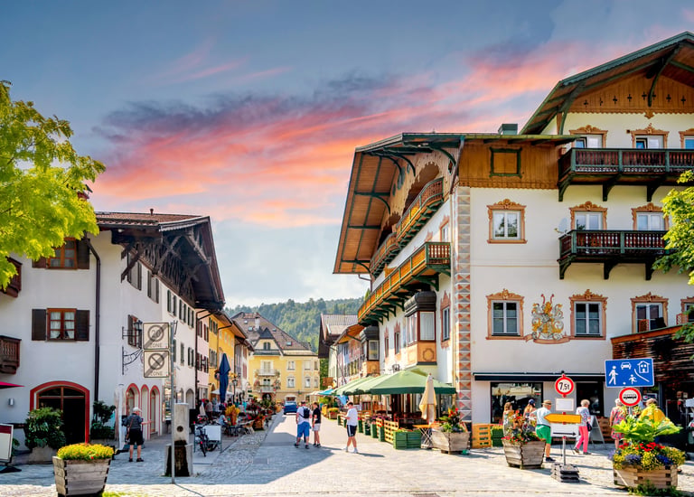 Charming Bavarian village street in Germany with traditional alpine architecture under a sunset sky.
