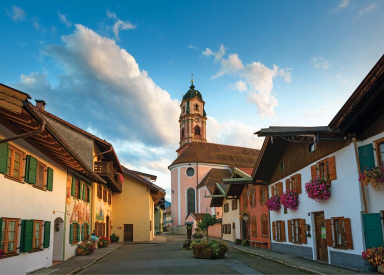 Traditional Bavarian houses with flower boxes lead to the historic St. Peter and Paul church in Mittenwald, Germany.