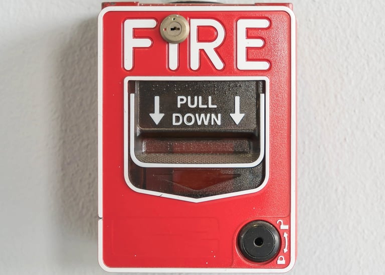 Estación manual roja de alarma contra incendios con texto blanco montada en una pared lisa.