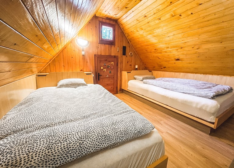 Cozy attic bedroom with two twin beds under a sloped wooden plank ceiling and walls.