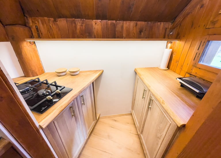 Rustic cabin kitchen featuring a gas stovetop, wood countertops, and light oak cabinets.