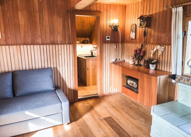 Cozy wooden cabin interior featuring a gray sofa, wood paneled walls, and a small fireplace.