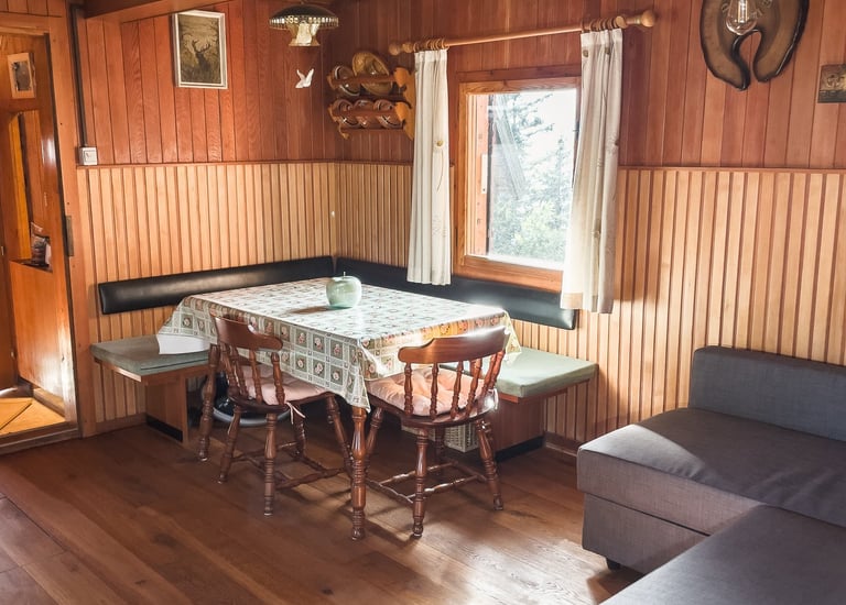 Rustic log cabin interior with wood paneled walls, a dining table with chairs, and a grey sofa.