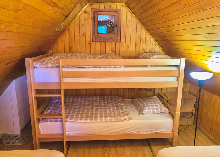 Rustic wooden attic bedroom featuring a light wood bunk bed with plaid bedding and a small window.