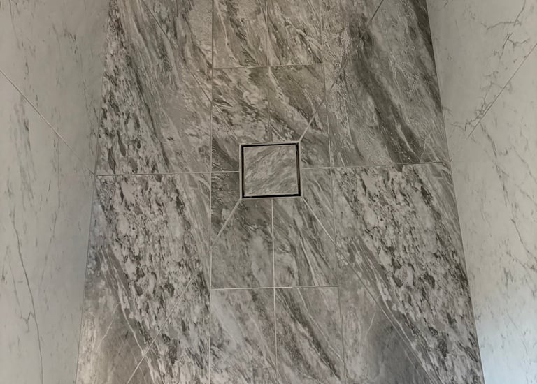 Modern bathroom shower featuring envelope cut floor tiles and a square center tile in drain.