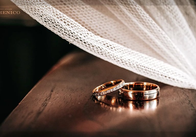 Alliances or rose et diamants sous voile de mariée en tulle, bois sombre.