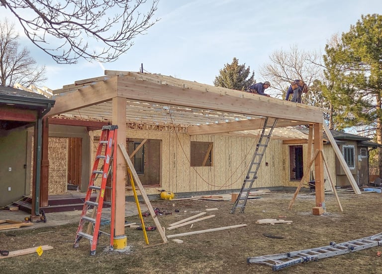 Framing progressing on a new home addition, showing wall sheathing and roof trusses by Elk Valley Contractors.