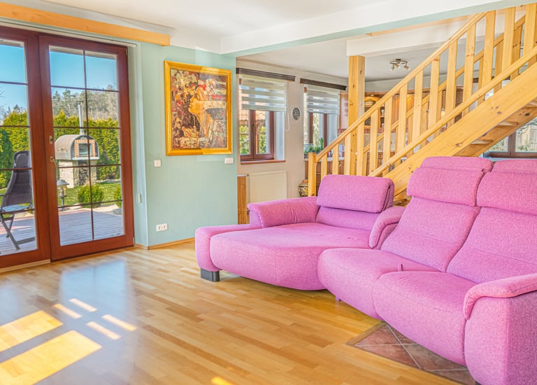 Modern living room featuring a bright pink sectional sofa, wooden staircase, and patio doors.