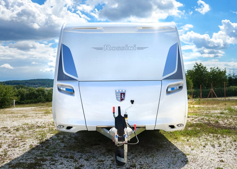 Front view of a white Tabbert Rossini luxury caravan parked on gravel under a blue sky.
