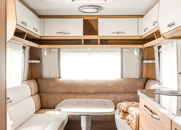 Modern luxury caravan interior with a neutral U-shaped dinette, adjustable table, and wood cabinetry.