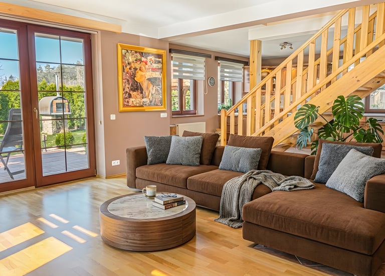 Modern living room with a brown sectional sofa, marble coffee table, and wooden staircase.