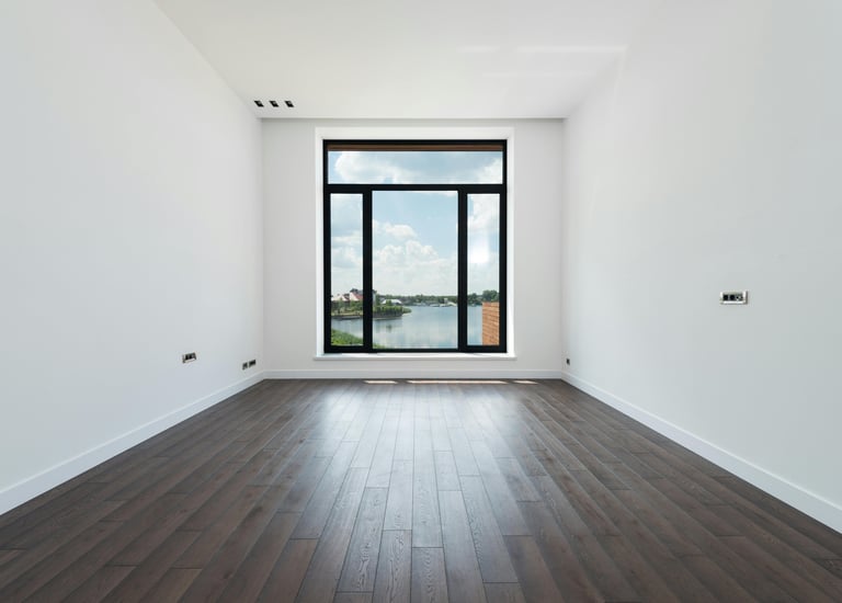 Empty modern room with dark hardwood floors and a large window overlooking a scenic lake.