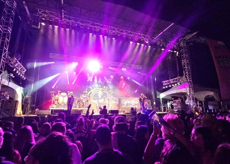 Cypress Hill performing live on a large outdoor concert stage with purple lighting and a cheering crowd.