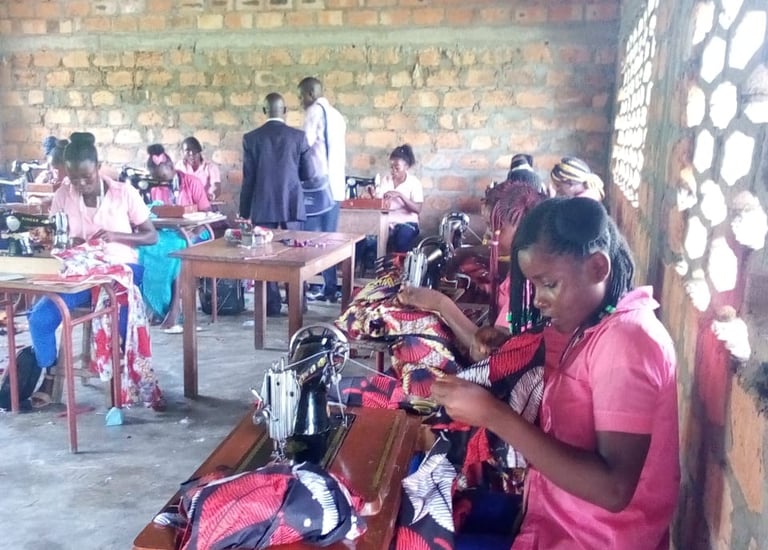 Students in a vocational training center learning tailoring and sewing skills using manual machines.