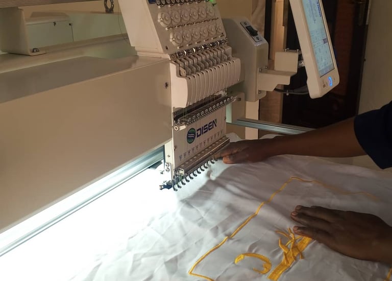 A professional operator using an industrial Disen computerized embroidery machine to stitch yellow designs on white fabric.