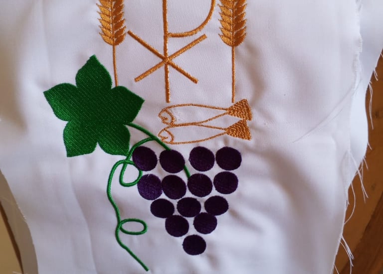 Embroidered white altar cloth featuring Chi Rho symbol, golden wheat stalks, and purple grapes.