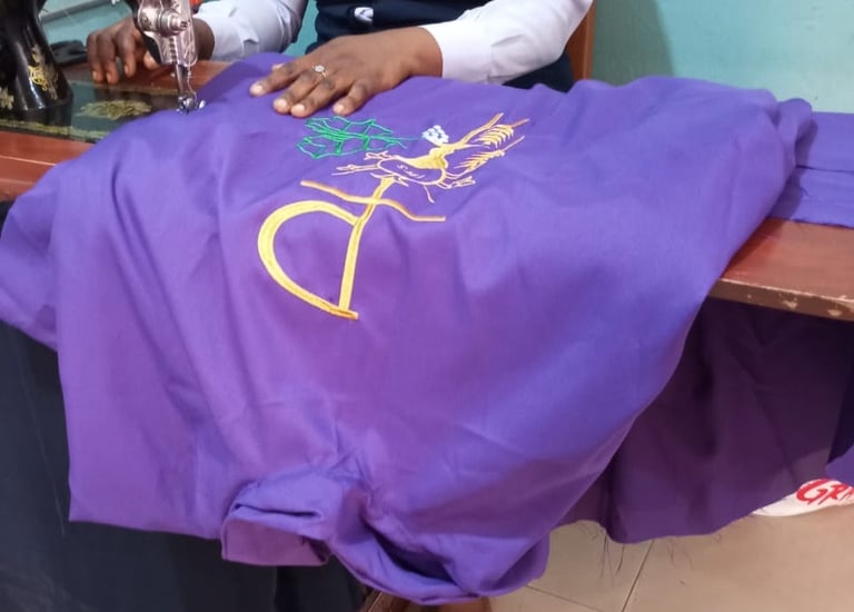 A tailor using a vintage sewing machine to embroider a gold religious symbol on purple fabric.