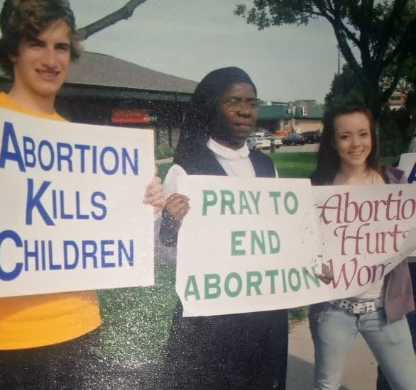 Three pro-life demonstrators including a nun holding anti-abortion signs at a public protest.