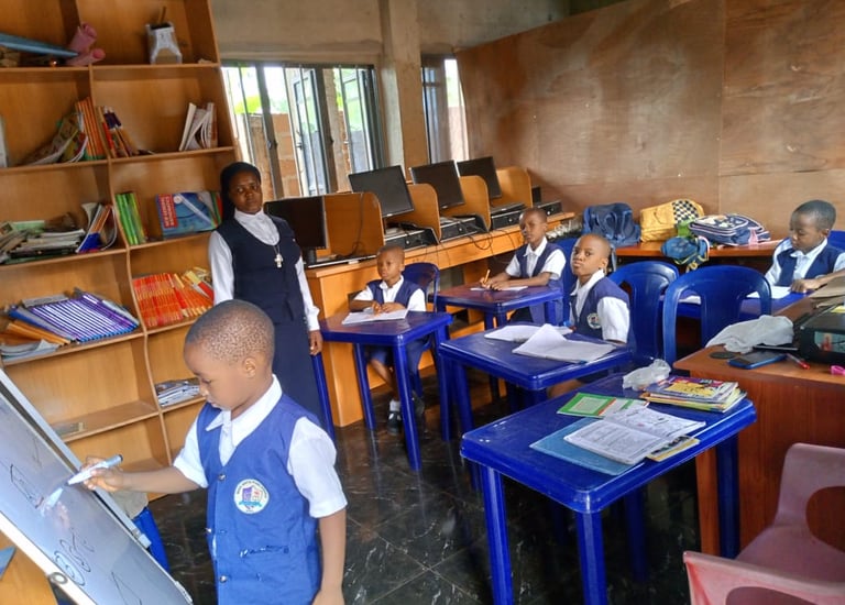 Students in uniforms learning in a classroom with a teacher, computers, and bookshelves.