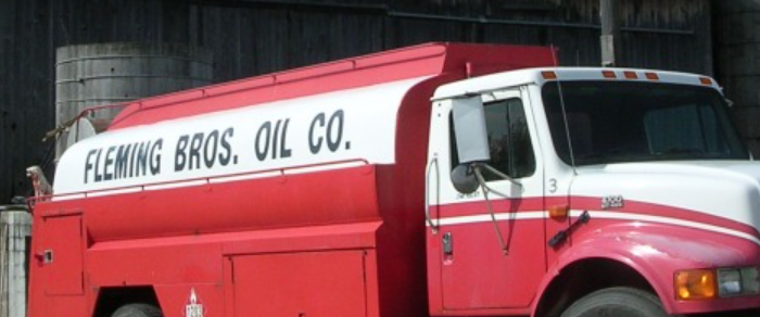 Red and white Fleming Bros. Oil Co. heating fuel delivery truck parked in front of a silo.