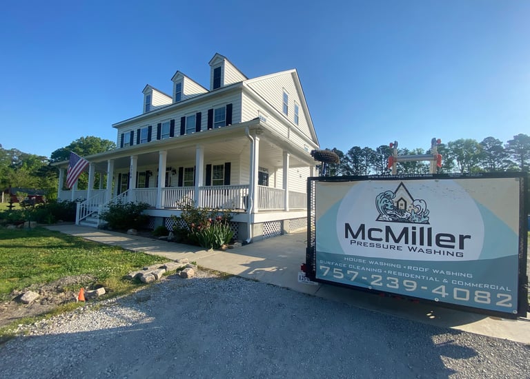 A McMiller Pressure Washing trailer parked in front of a clean white two-story residential home with a large porch.