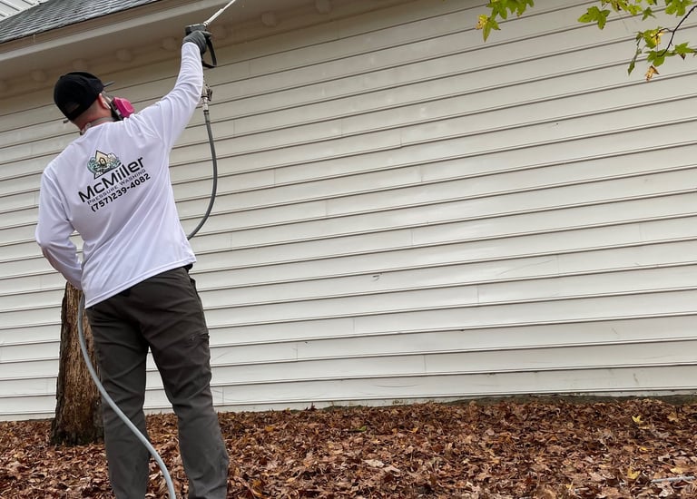 Professional contractor soft washing white house siding and roof to remove algae and stains.