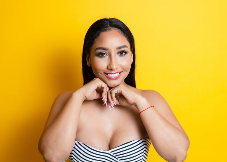 Smiling woman in her 30s and long dark hair posing against a vibrant yellow background.