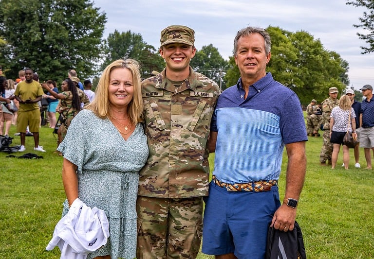 Two parents standing with their son who is in Army camoflage.  They are with other families.