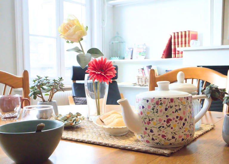Table conviviale avec théière, fleurs et vaisselle dans logement meublé pour professionnels.