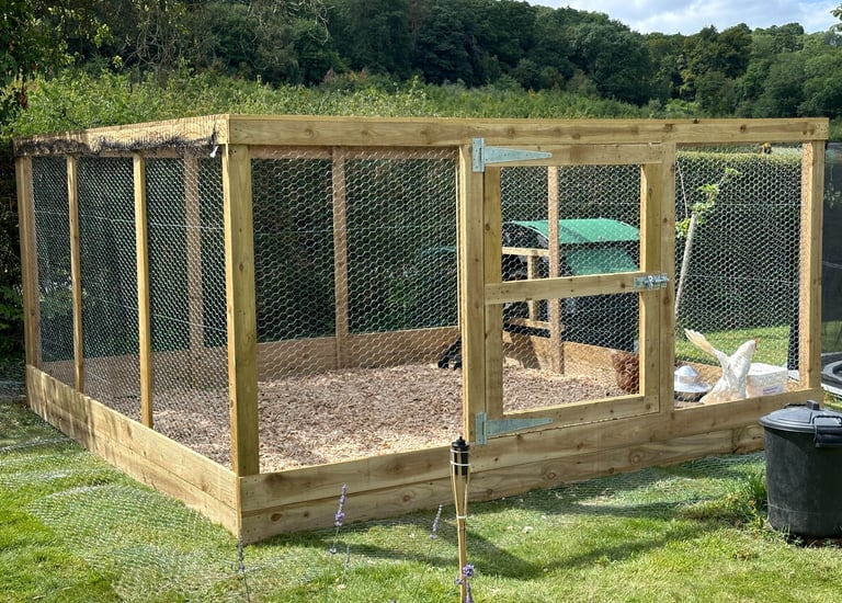Large wooden chicken run with wire mesh and a secure gate for poultry protection in a garden.