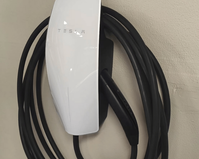 White Tesla Gen 3 Wall Connector home EV charging station mounted on a wall with cable coiled.