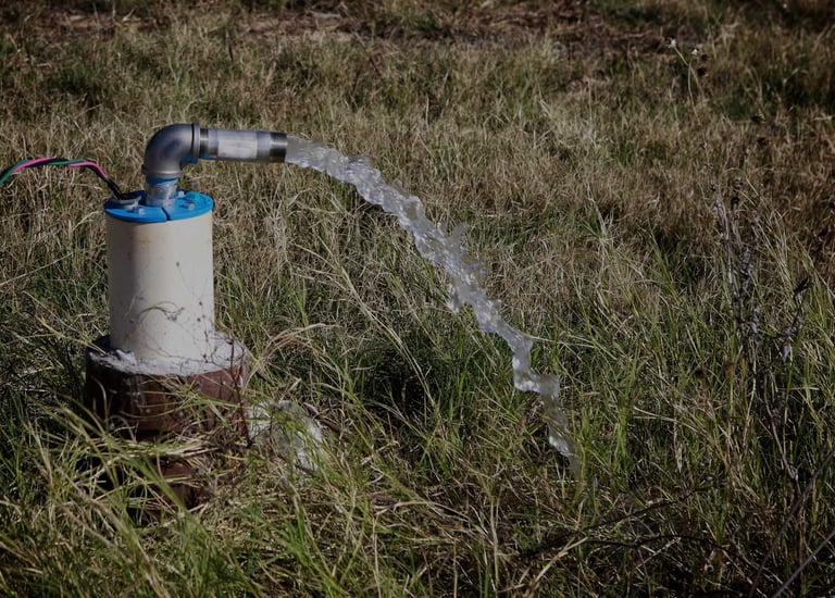 Electric submersible water well pump discharging a stream of clear water into a grassy field.