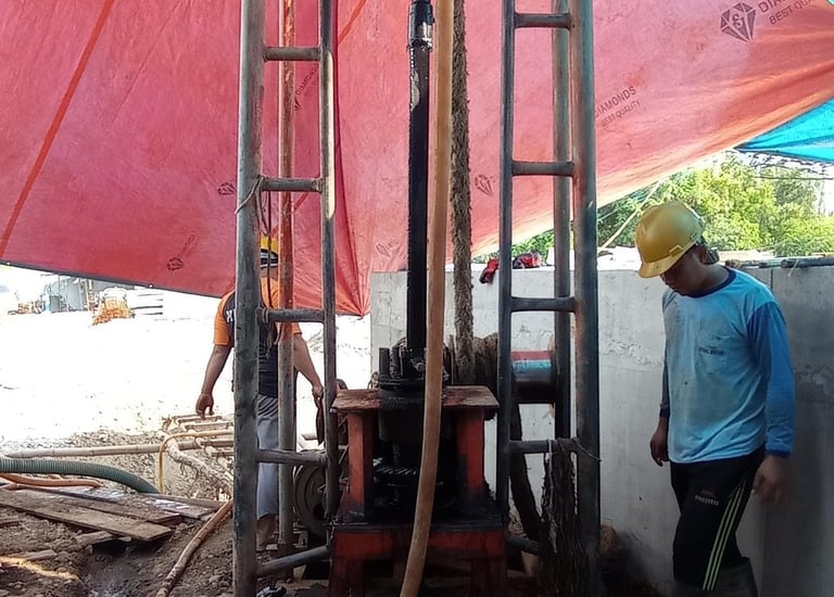 Construction workers operating a water well drilling rig at a construction site with red tarp.
