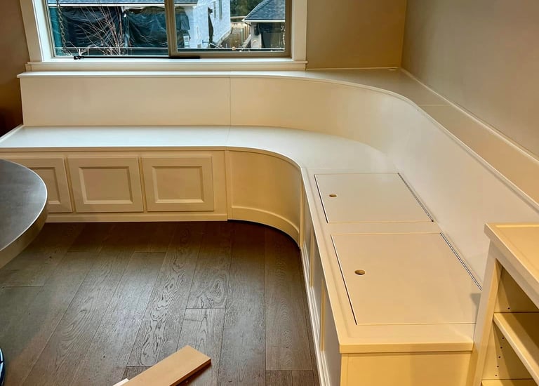 Custom white built-in corner banquet seating with integrated storage on dark wood floors.