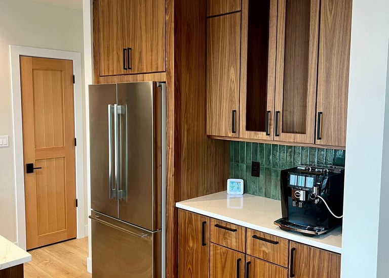 Modern kitchen with wood cabinets, stainless steel refrigerator, and a coffee maker on white counters.