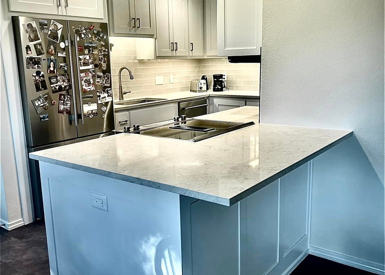 Modern white kitchen with marble countertops, stainless steel appliances, and shaker cabinets.
