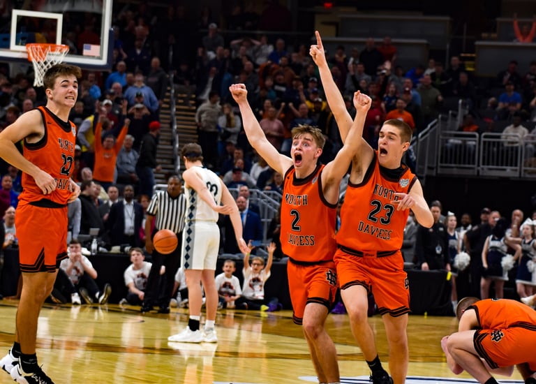 North Daviess high school basketball players win in orange jerseys celebrate a victory on the court.