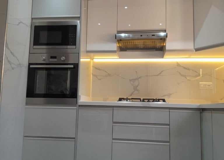Modern gray and white gloss kitchen cabinets with marble backsplash and LED under-cabinet lighting.