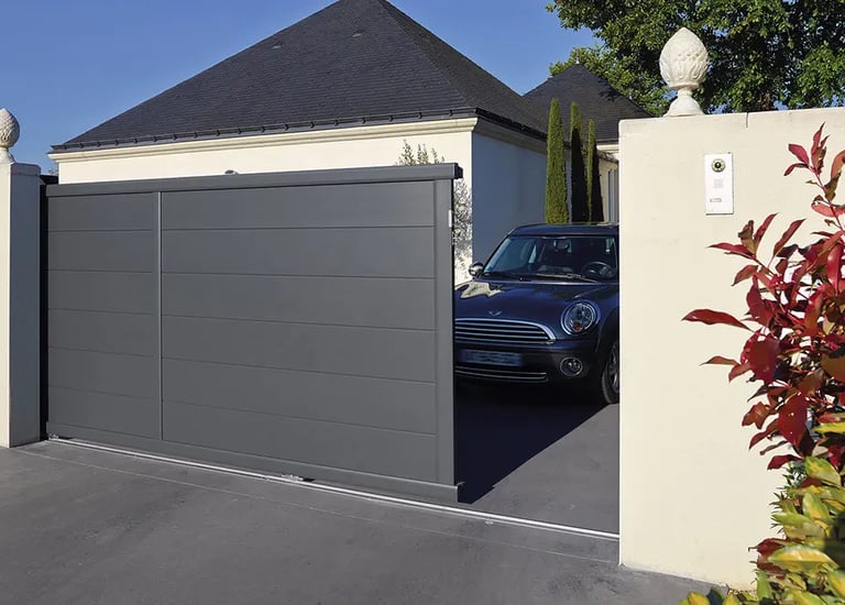 Automatic grey aluminum sliding gate opening to reveal a car parked in a modern home driveway.