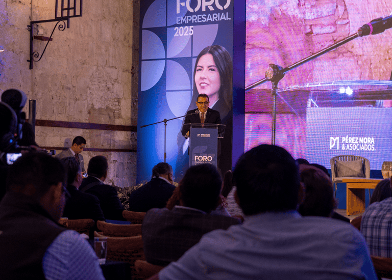 Speaker at Foro Empresarial 2025 business conference podium addressing a seated audience in an auditorium.
