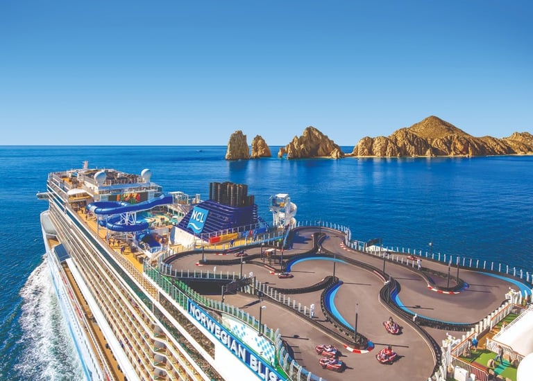 Norwegian Bliss cruise ship featuring a top-deck go-kart race track near coastal rock formations.